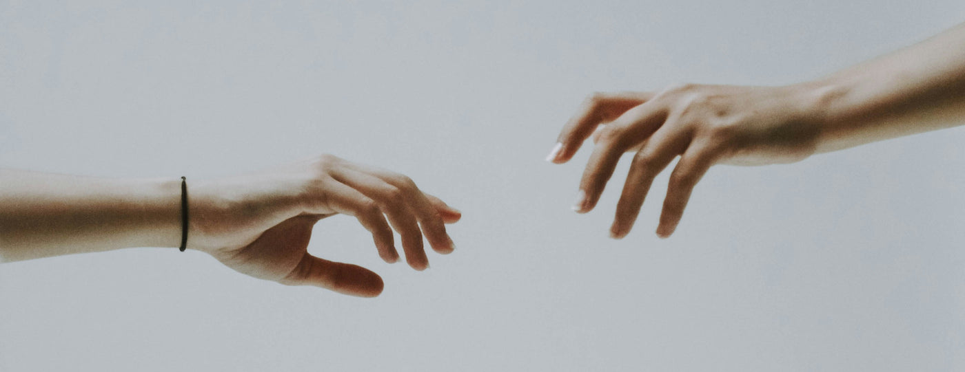 Two hands reaching towards each other against a plain background