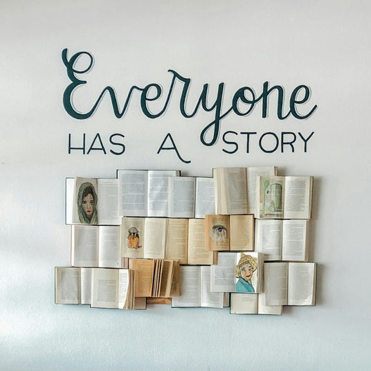 “Artful wall display with open books and the words ‘Everyone Has a Story,’ symbolizing the personal meaning behind thoughtful gifts.”