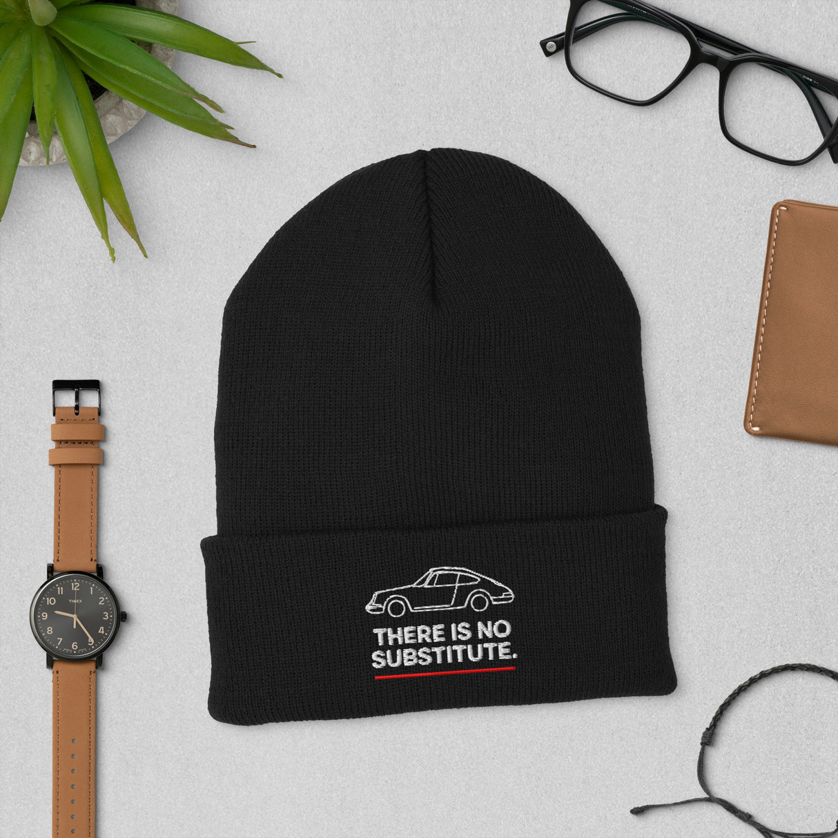Black cuffed beanie embroidered with Porsche 911 outline and “There Is No Substitute” text, styled flat lay.