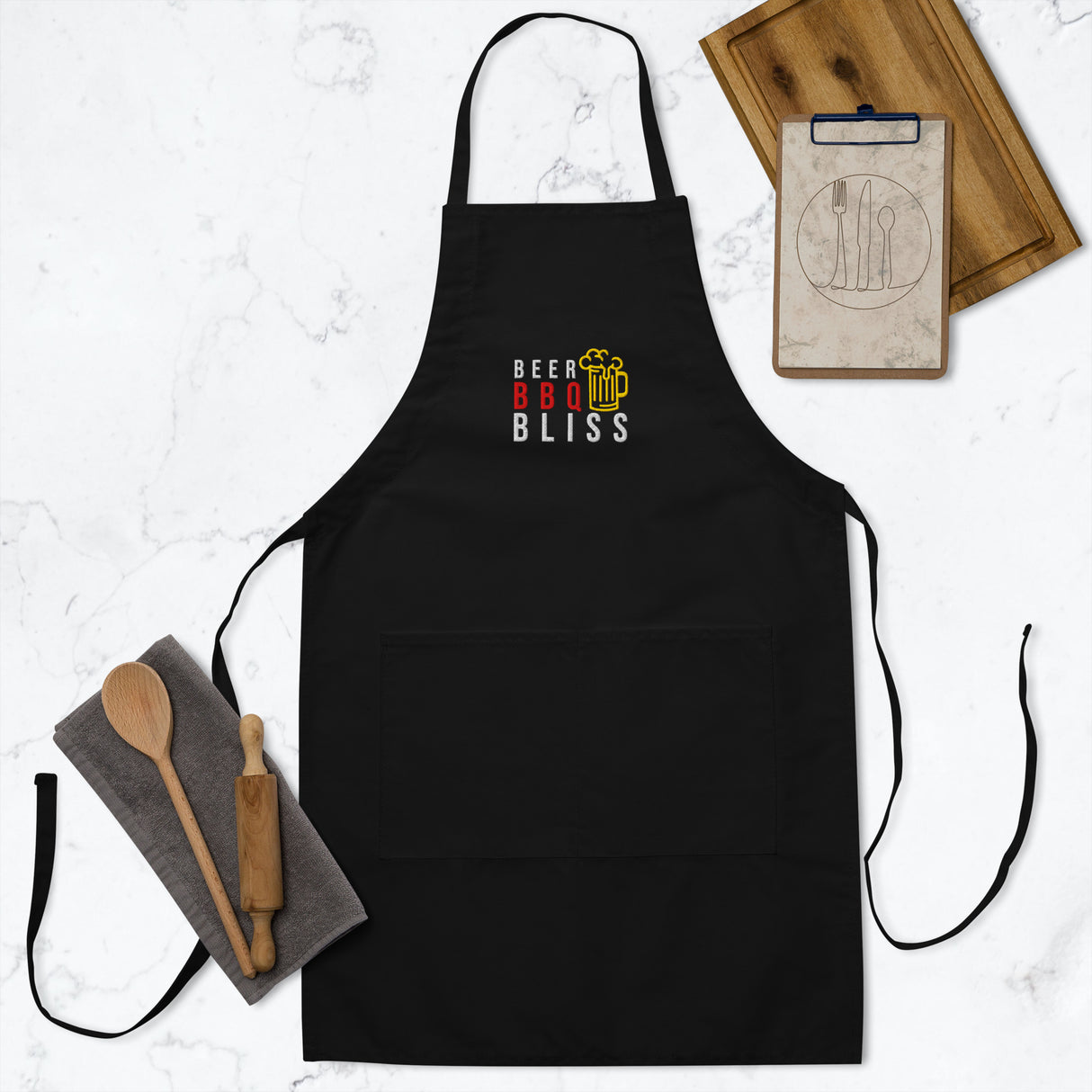 Black apron with 'Beer BBQ Bliss' text on a white surface with kitchen items.