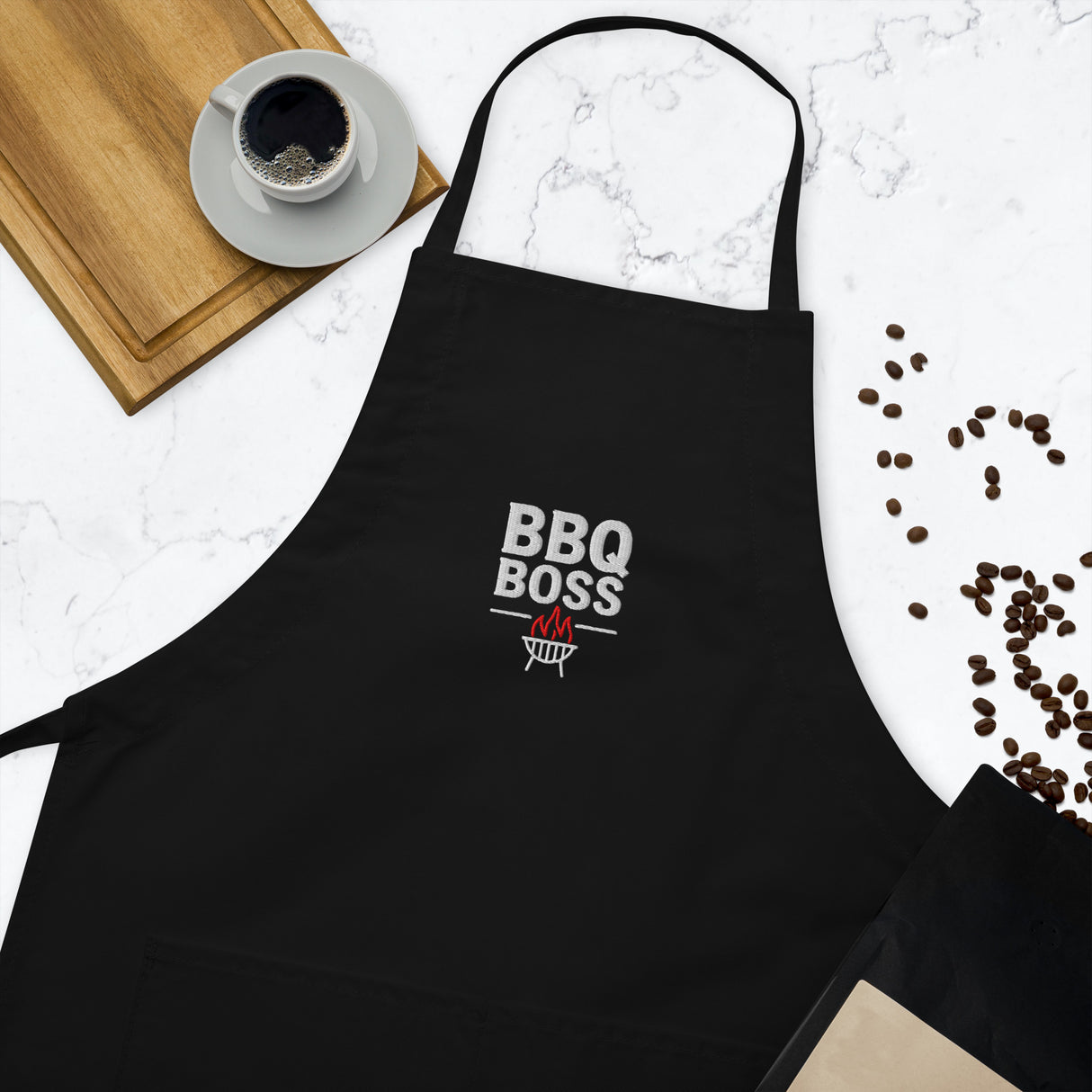 Black apron with 'BBQ Boss' text on a kitchen counter with coffee and beans.