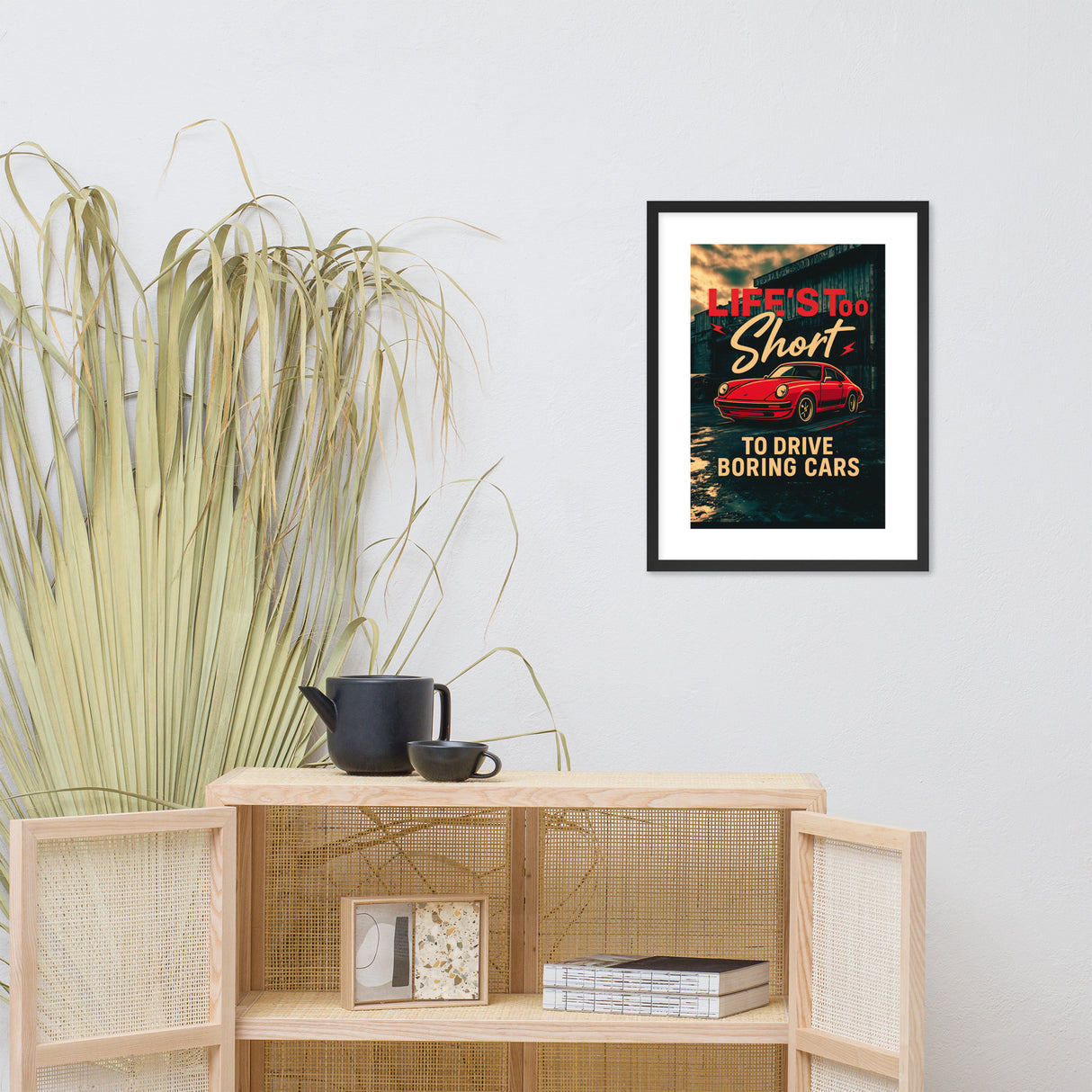 Framed poster with a red porsche and text on a wall above a wooden shelf with decor items.