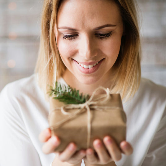 "Smiling woman holding a small gift wrapped in brown paper and tied with twine, looking down warmly with joy and appreciation."