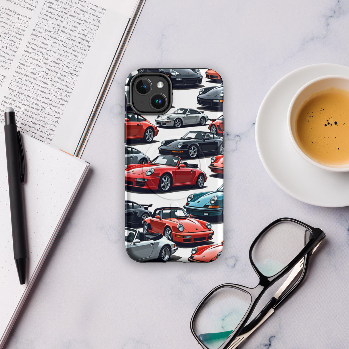 Phone case with car design on a marble surface with a book, pen, and coffee.