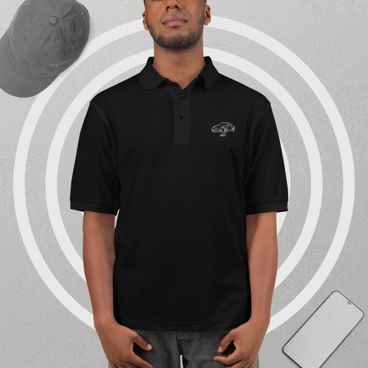 Black premium polo shirt with embroidered Porsche outline logo, worn by male model in relaxed modern setting