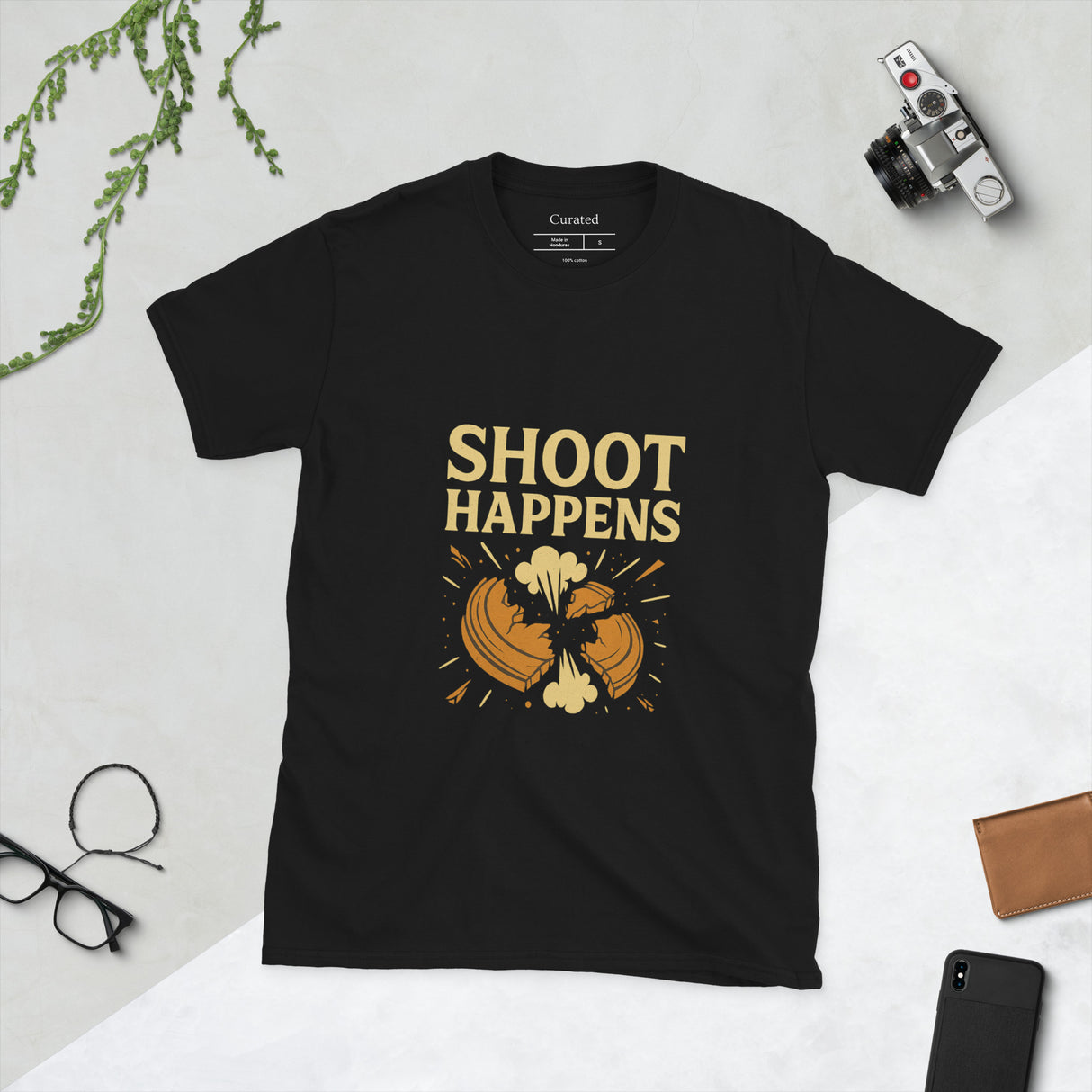 Black t-shirt with comic-style exploding clay target and text reading "Shoot Happens"