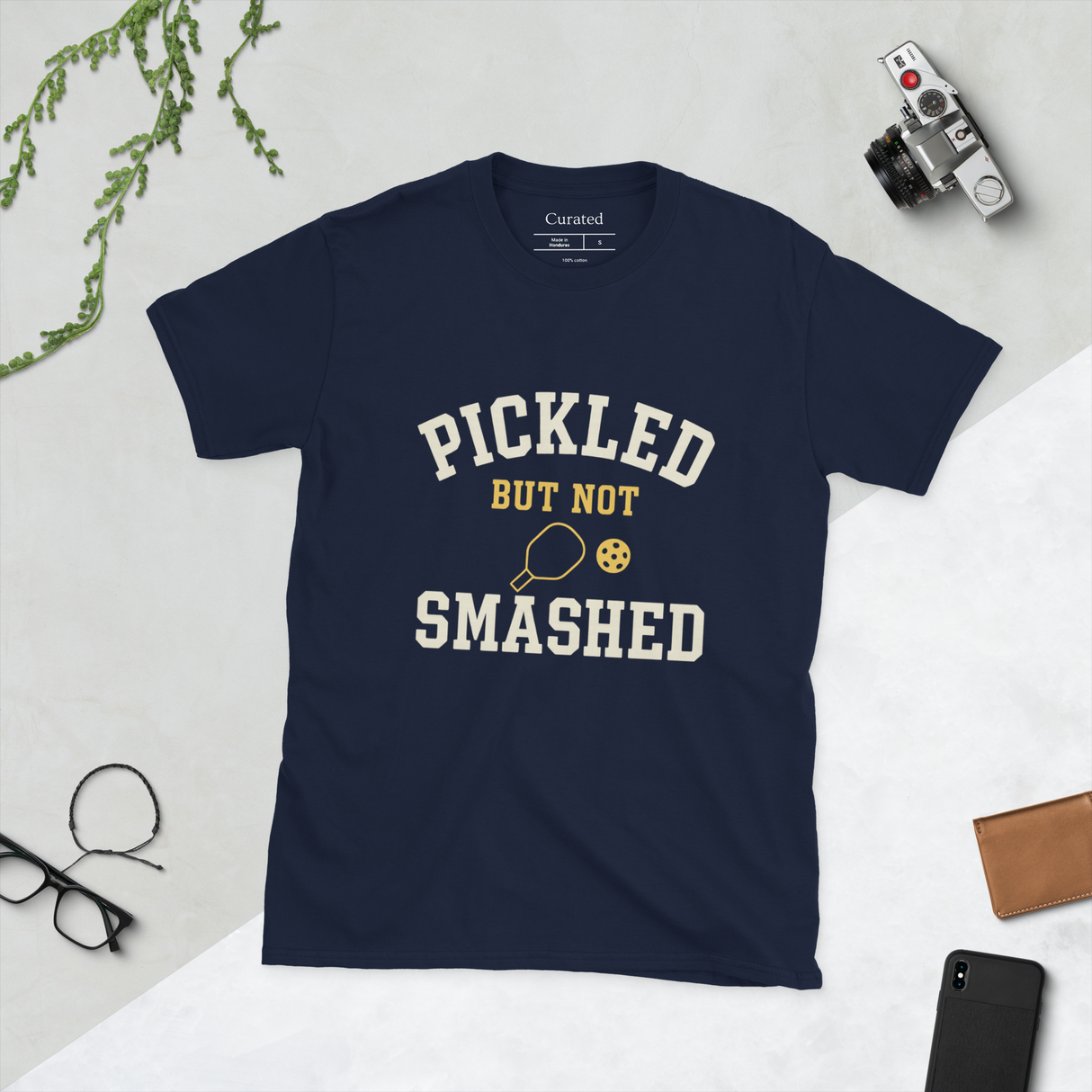 Navy blue t-shirt with 'Pickled But Not Smashed' text on a light gray surface with accessories.