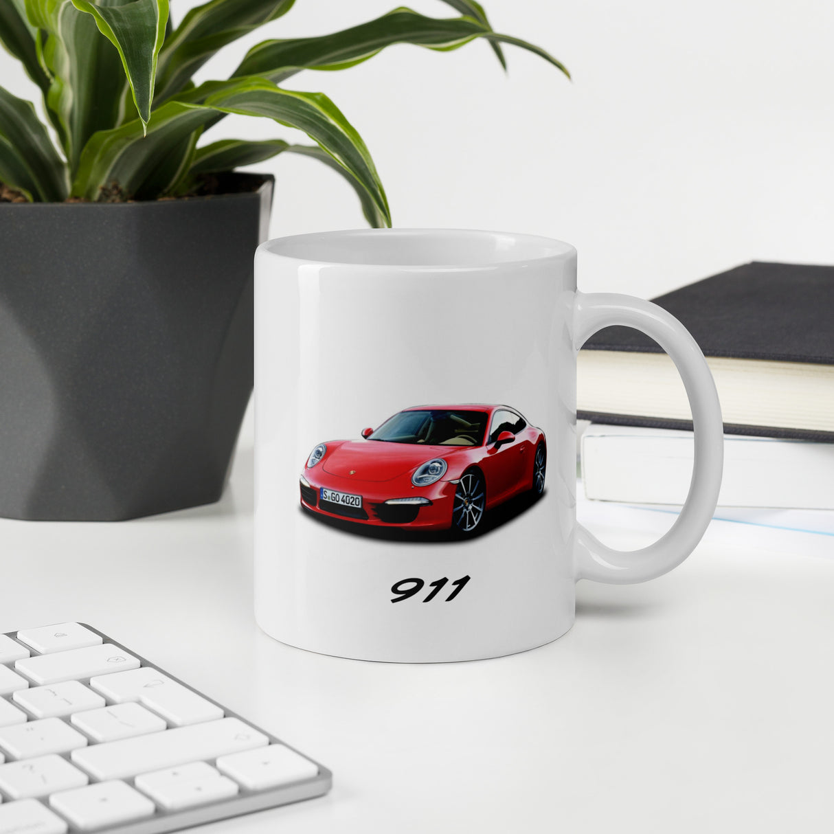 "White glossy mug featuring a red Porsche 911 car image and '911' text, shown on a stylish desk next to a keyboard and plant"
