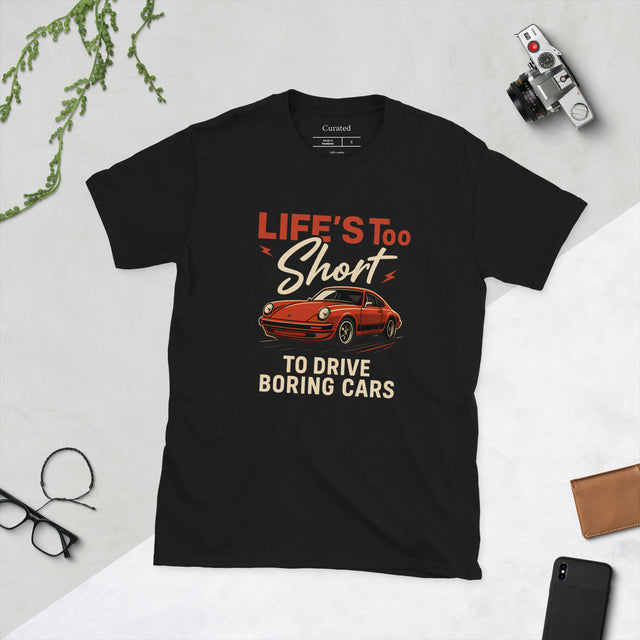 Black unisex t-shirt featuring bold red Porsche 911 graphic with the phrase “Life’s Too Short to Drive Boring Cars.”